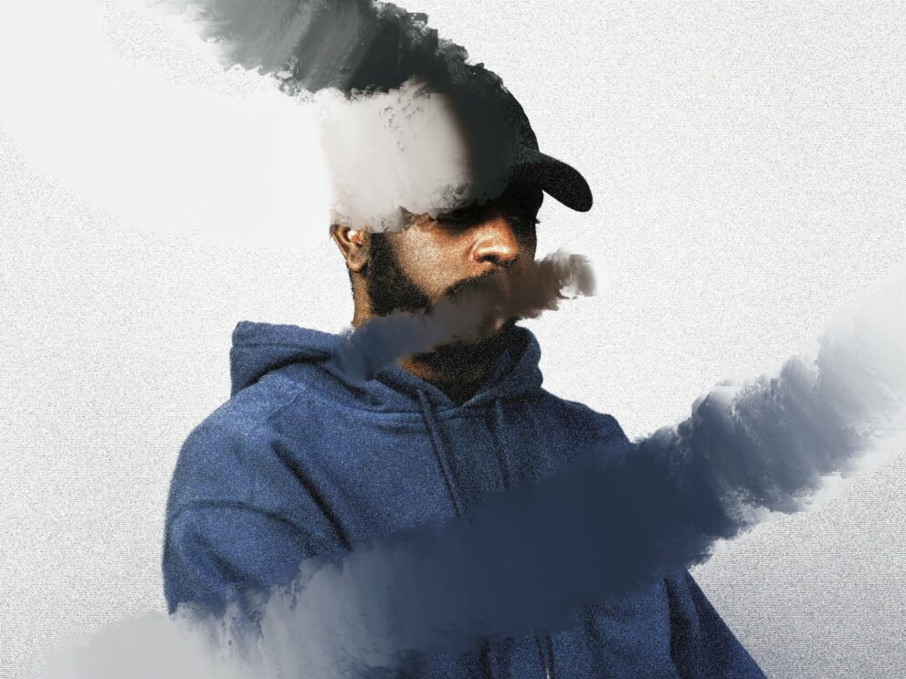 Stylized photo of Alfa Mist. The portrait shot of the artist wearing a blue hoodie and a black baseball cap is edited with bush strokes blurring the colors over his face.