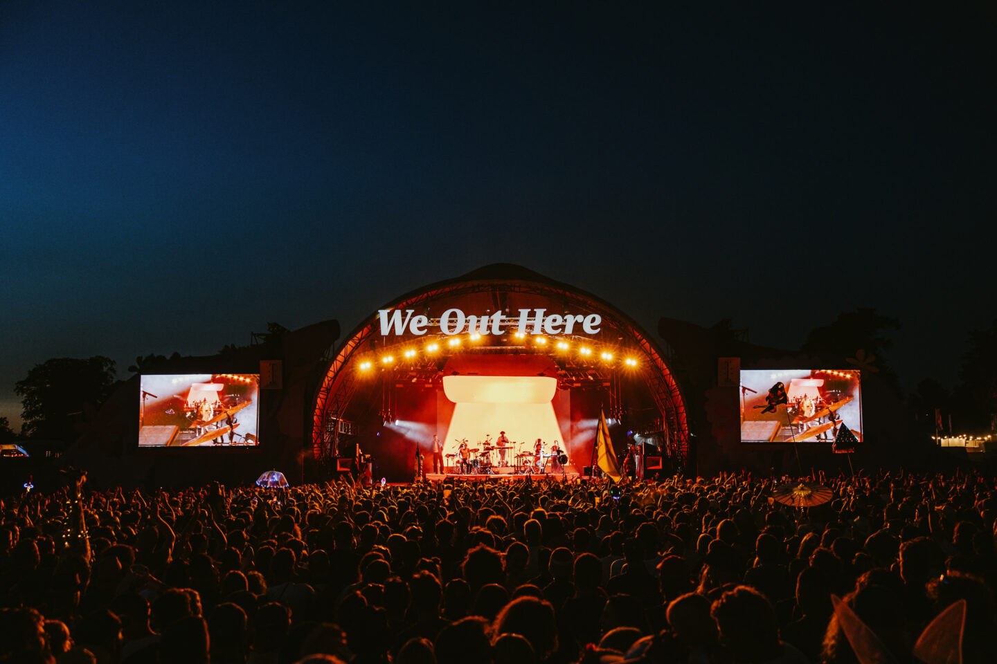 the we out here festival stage in bright light against the darkness of the night with crowds of people gathering in front