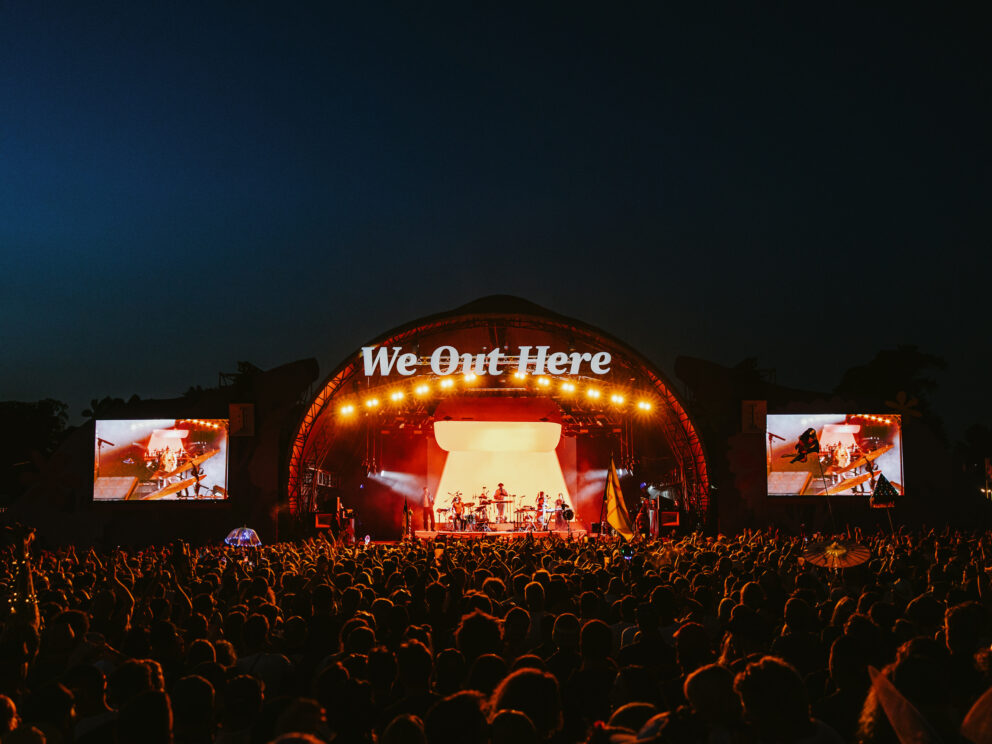 the we out here festival stage in bright light against the darkness of the night with crowds of people gathering in front