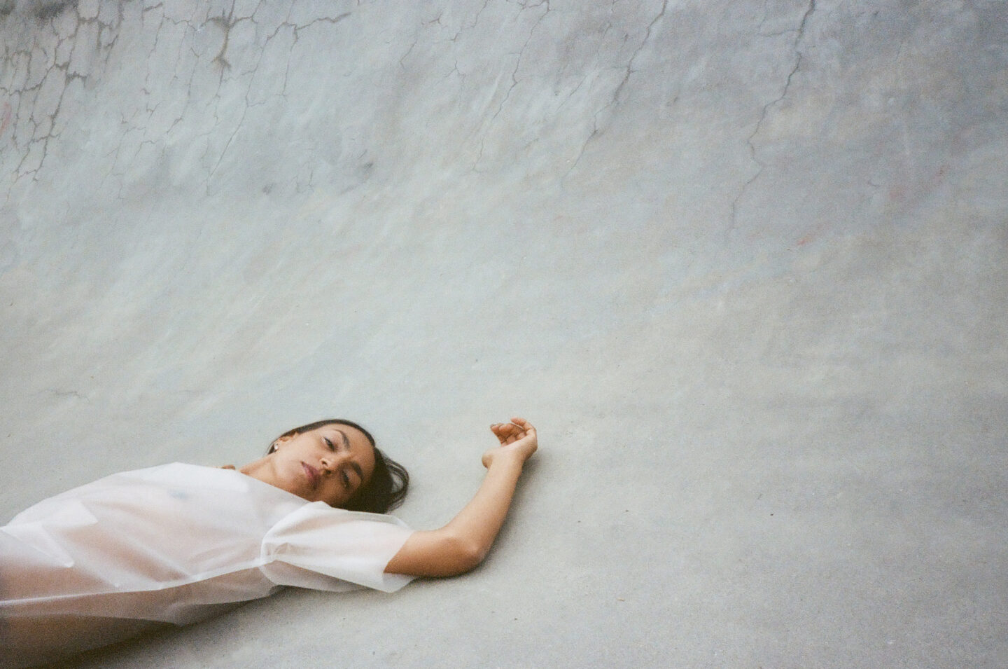 A woman lying on concrete floor with her arm stretched above her heard. She is in the bottom left corner of the image. Her legs are cropped out.