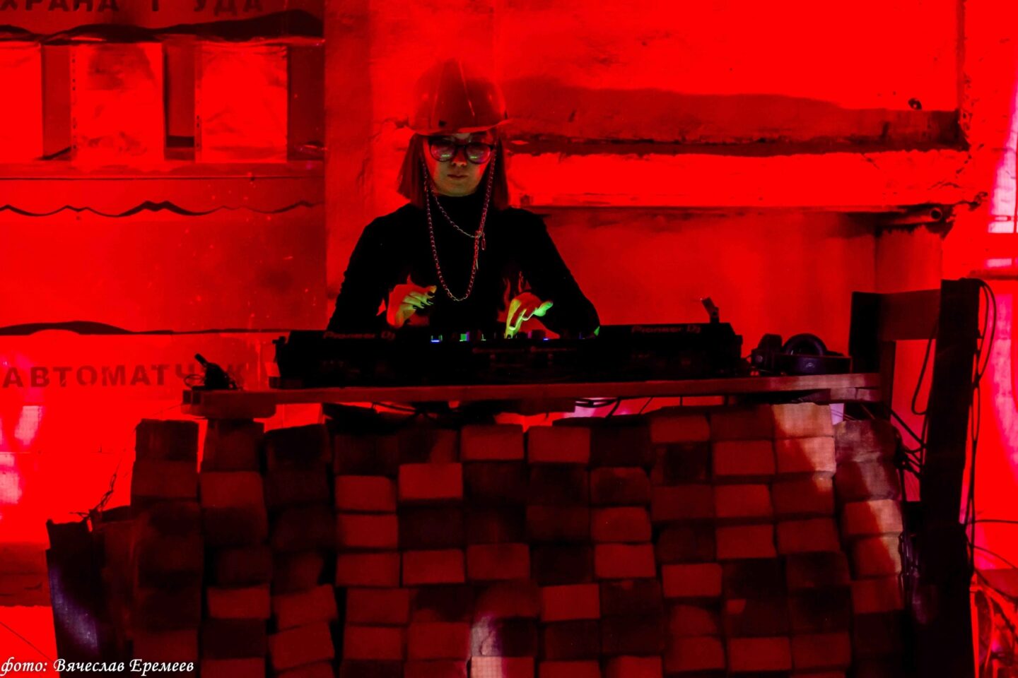 Lit in red, a Dj is standing behind a pult built of bricks